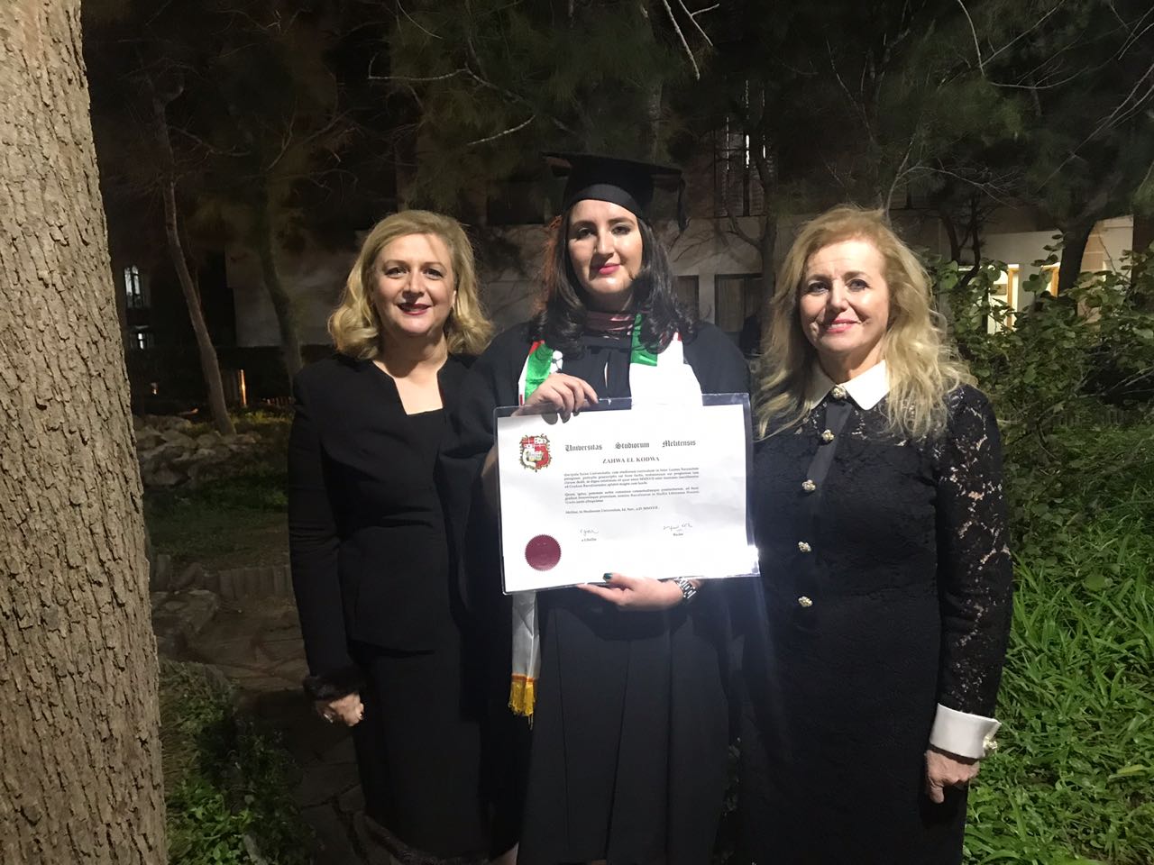 Zahwa Arafat in cap and gown at her University of Malta graduation, holding her diploma, a Palestinian flag stole on her shoulders